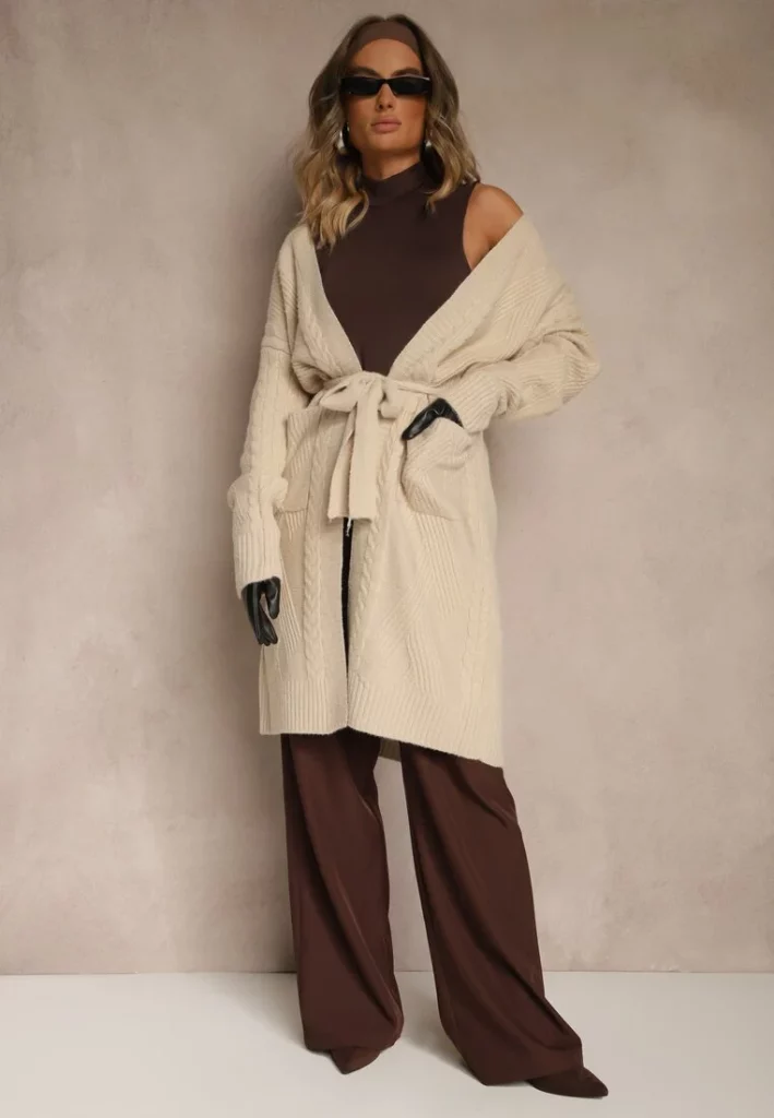 Modelka prezentuje beżowy kardigan z paskiem w stylizacji z brązowymi spodniami i topem oraz okularami przeciwsłonecznymi.
