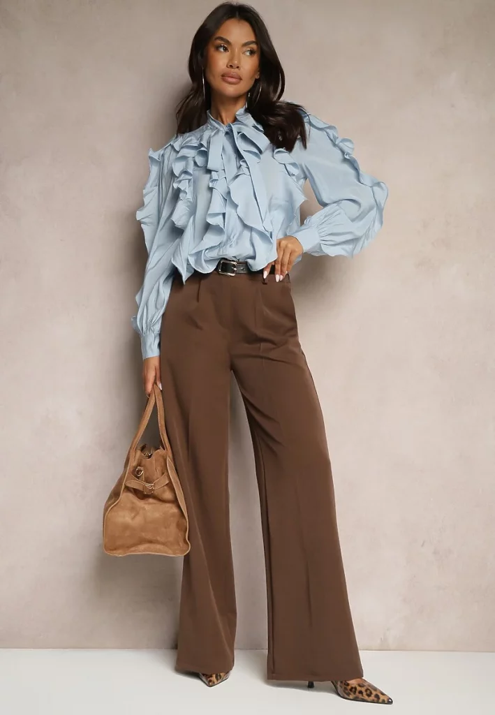 Modelka prezentuje stylizacje z bufiastą błękitną koszulą i garniturowymi brązowymi spodniami