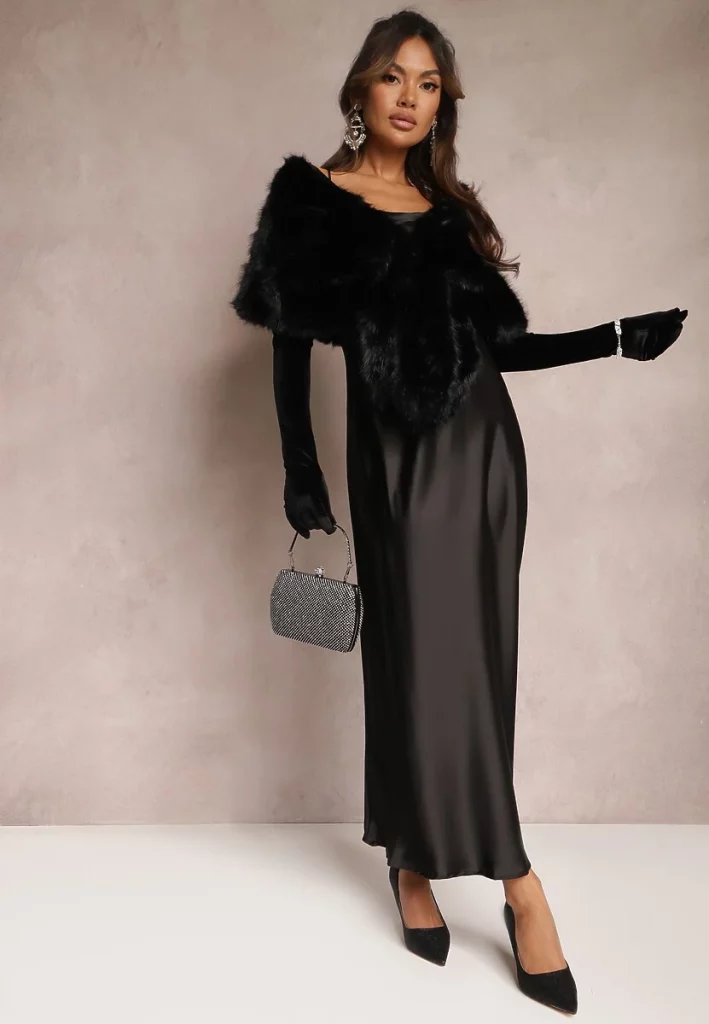 Modelka prezentuje wieczorowy total look w kolorze czarnym z satynową sukienką maxi, szpilkami, futrzaną etolą i błyszczącą torebką.