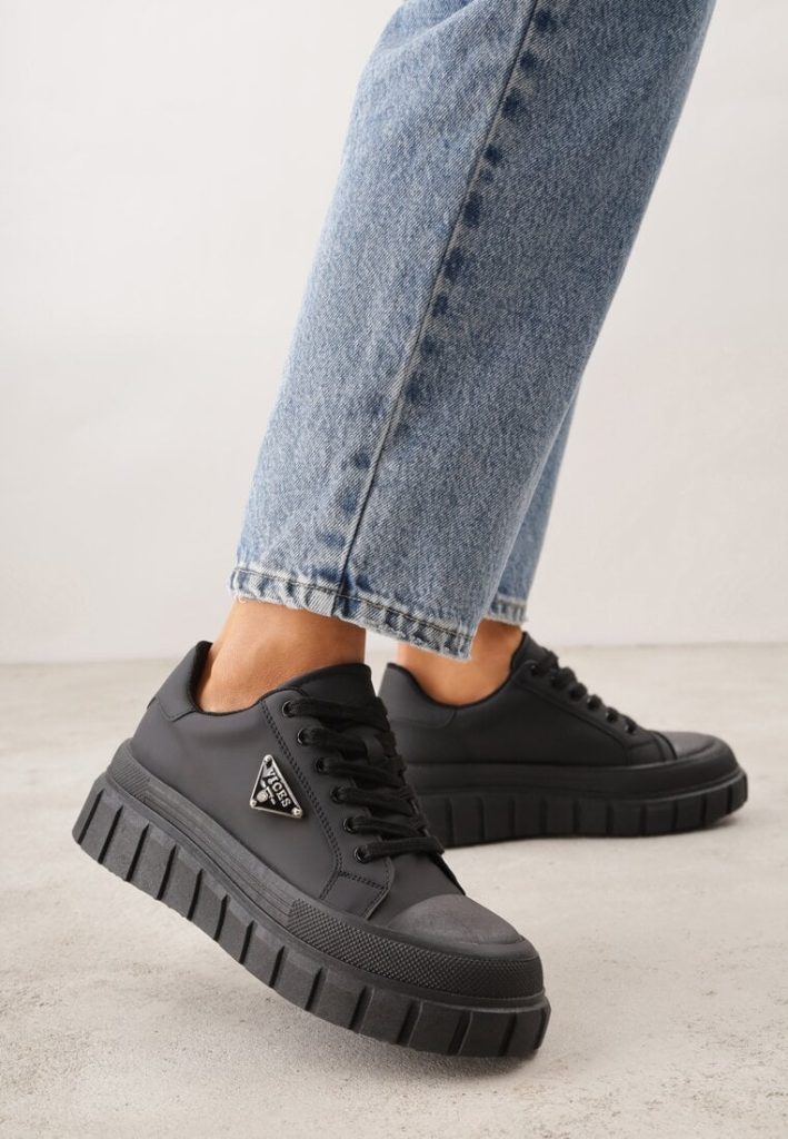 Modelka prezentuje czarne sneakersy VICES na grubej podeszwie z jasnymi jeansami