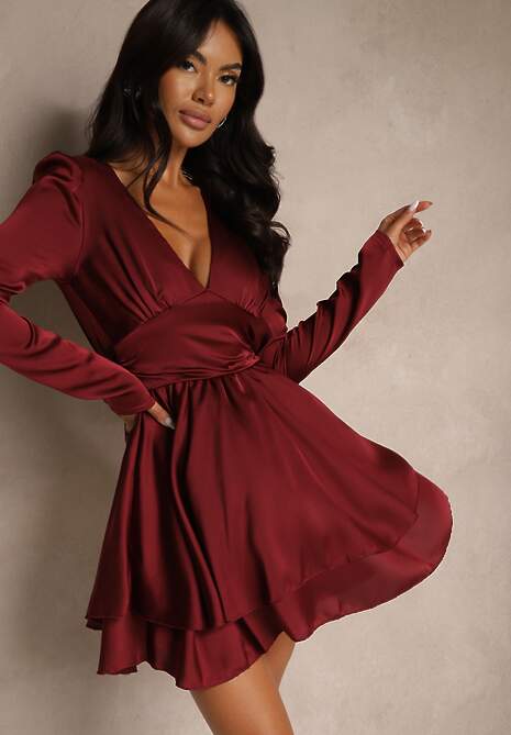 Modelka prezentuje bordową satynową sukienkę mini z długimi rękawami.