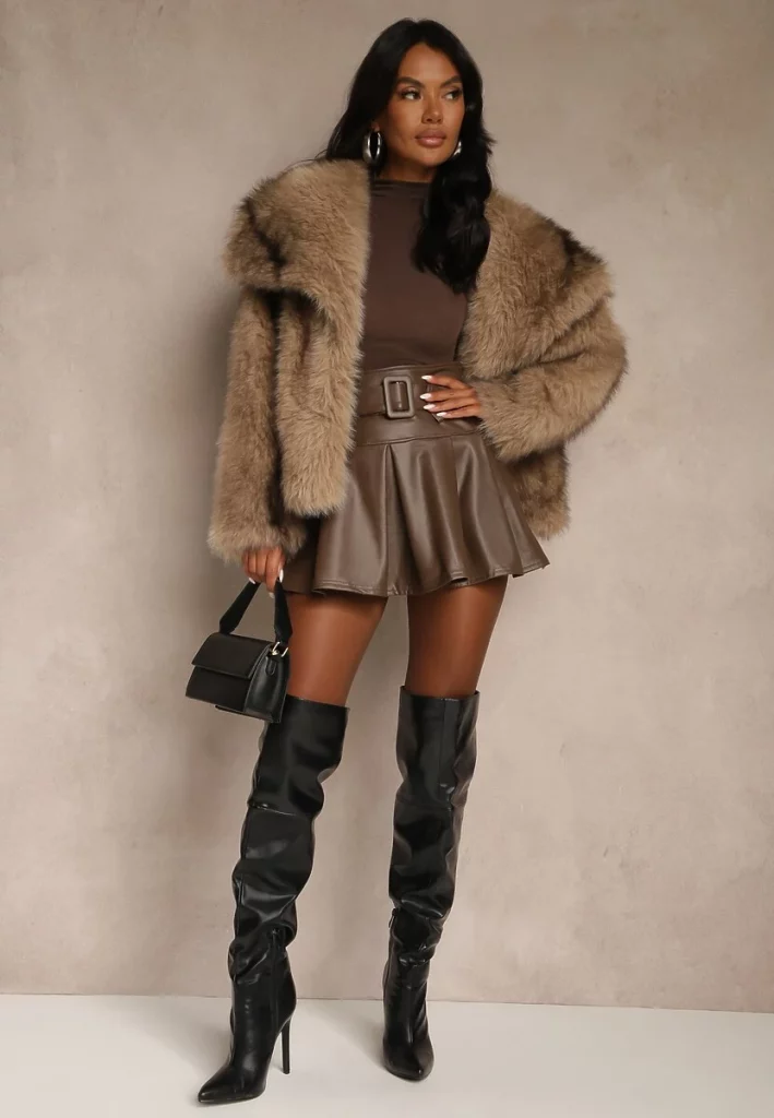 Modelka prezenuje krótkie jasnobrązowe futerko skomponowane z brązowym topem i spódnicą oraz czarnymi kozakami i torebką.