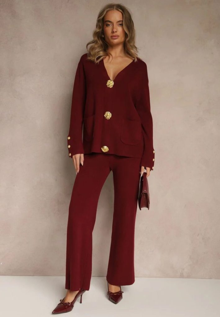 Modelka prezentuje dzianinowy set w kolore bordowym z eleganckimi guzikami, bordowe szpilki i bordową torebkę.