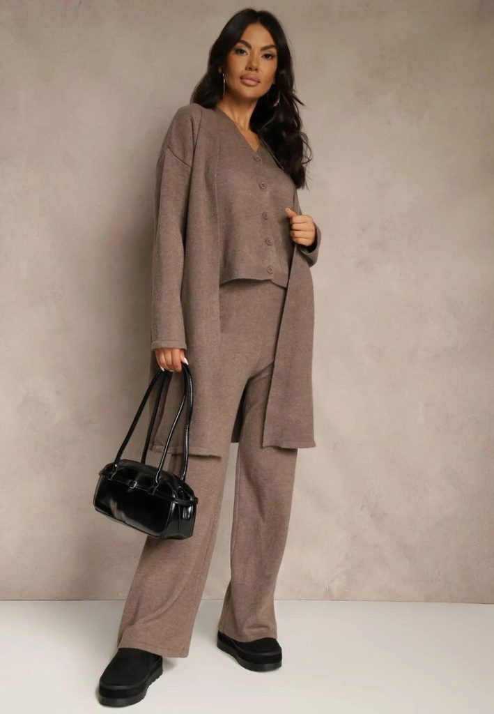 Modelka prezentuje beżowy dzianinowy komplet z kamizelką, długim kardiganem i spodniami wide leg w połączeniu z torebką bowling i śniegowcami.