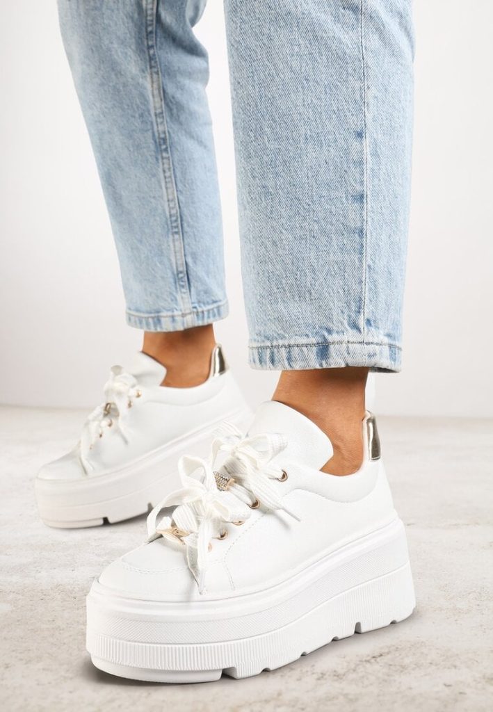 Białe sneakersy z metalicznymi ozdobami na płaskiej podeszwie, widok z boku.