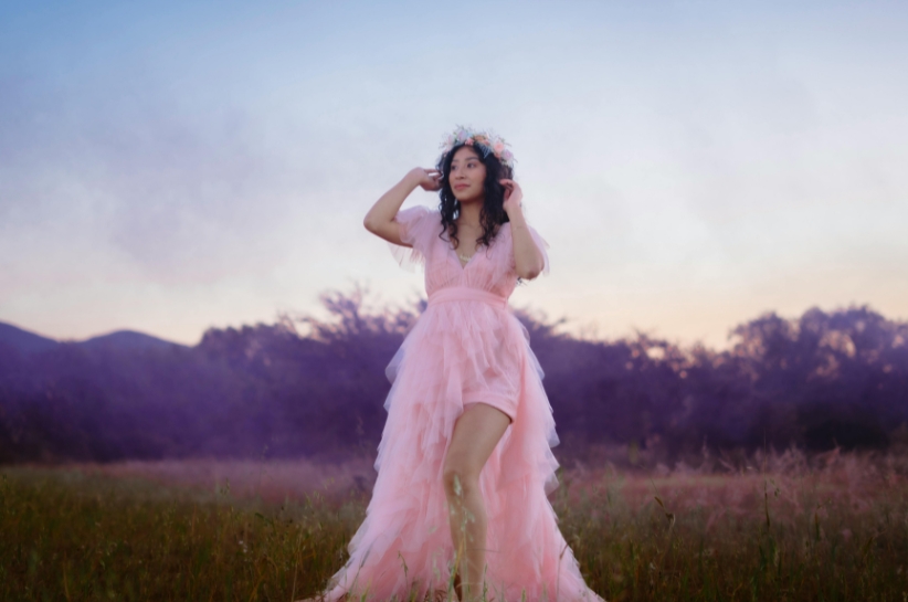 Modelka na tle przyrody prezentuje pasteloworóżową sukienkę o fasonie princeski.